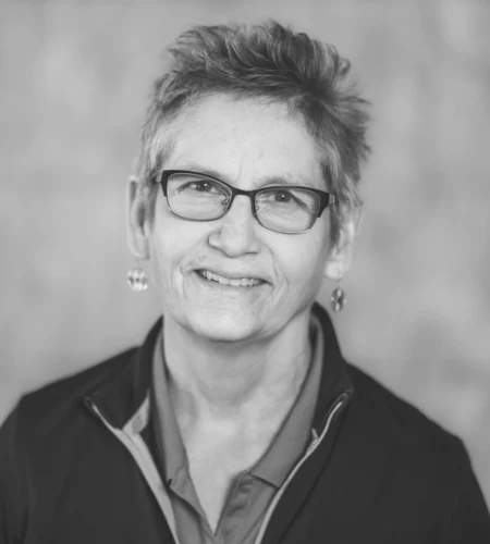 A black and white photo of Dondi Szombatfalvy, a woman wearing glasses, looking thoughtfully at the camera.