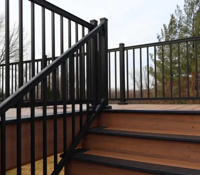 A wooden deck featuring a black railing and steps leading down.