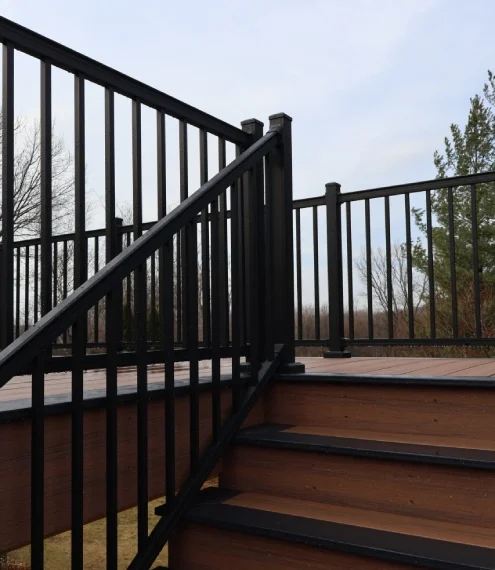 A black railing surrounds a wooden deck, leading down to steps made of the same wood material.